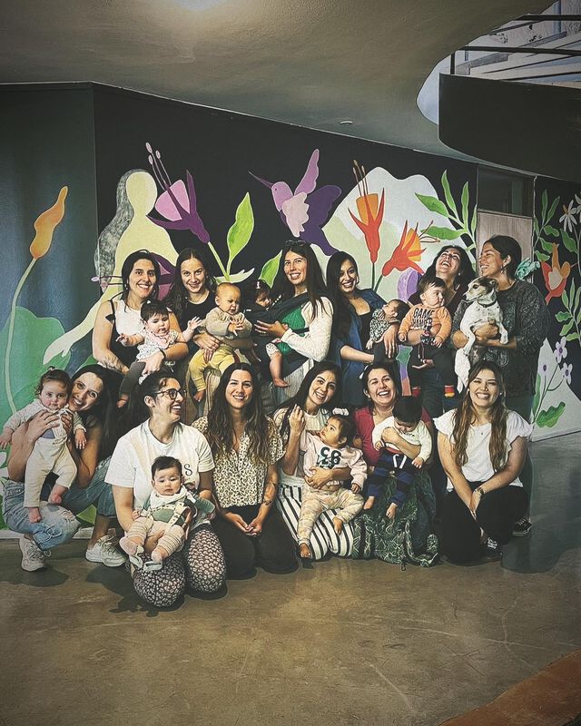 Mamás con sus bebés frente a un mural de flores, después de un encuentro de puerperio